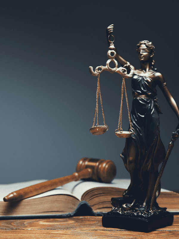 Statue von Dike – der Göttin des Rechts, Richterhamme und ein offenes Gesetzbuch auf einem Tisch